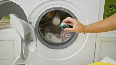 Temiz bir odanın içinde, modern bir çamaşır makinesinde çamaşır yıkarken bir insanın elinde deterjan kapsülü tutarken..