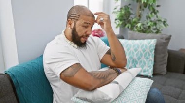 Sıkılmış ve yorgun Afrika kökenli Amerikalı bir adam, kollarını kavuşturup kanepede oturur, düşüncelere dalmış, evdeki sorunlarla boğuşur..