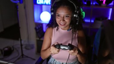 Canlı bir İspanyol flaması, oyunlara dalmış bir gece. Güzel genç bir kadın oyun bahçesinde joystick ile video oyununda ustalaşıyor, oyun odasından canlı yayın yapıyor..