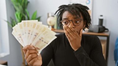 Şok olmuş genç siyahi kadın, ağzı kapalı, Danimarka kronu banknotları tutan, hata üzerine şaşkınlık ve korku ifade ediyor.