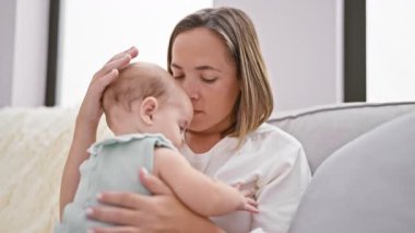 Rahatlamış anne ve kızı güzel bir öpücüğü paylaşıyorlar, birlikte oturma odasındaki kanepede oturup aile sevgisini ifade ediyorlar.