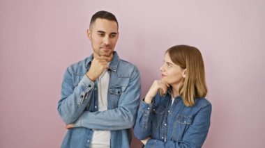 Kot gömlekli güzel bir çift, elleri çenelerinde pembe izole bir arka planda duruyorlar. Düşünceli yüzler şüpheyle dolu, kafa karıştırıcı bir soru üzerinde kafa yoruyor, derin düşüncenin bir resmi..