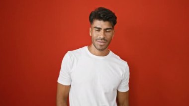 Beyaz tişörtlü yakışıklı, genç, İspanyol bir adam canlı kırmızı bir arkaplan karşısında çeşitli ifadeler sergiliyor..