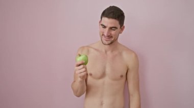 Genç İspanyol üstsüz bir adam bir fikir veya soruyla gülümseyen bir elma tutuyor mutlu bir yüzle işaret ediyor, pembe arka planda bir numara.