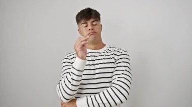 Genç, stresli, çizgili gündelik giysili, kollarını göğsünde kavuşturan, çok düşünen, sıkıntı ve depresyon belirtileri gösteren, beyaz bir arka planda izole edilmiş bir İspanyol.