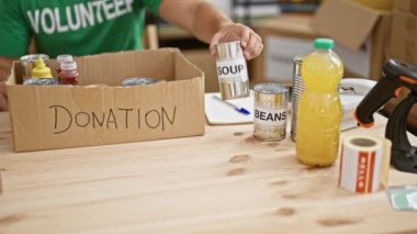 Yeşil gönüllü tişörtlü genç bir adam bir hayır etkinliğinde içeride yiyecek bağışları organize ediyor..