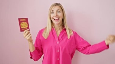 Neşeli genç sarışın kadın gururla kendini işaret ediyor. Kuzey İrlanda pasaportu ile izole edilmiş pembe bir arka planda. Kendinden emin, iyimser bir gülümseme sergiliyor..