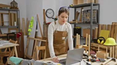 Bir kadın ve bir erkek, bir dizüstü bilgisayar kullanarak marangozluk atölyesinde iş birliği yapıyor ve marangozluk planlarını tartışıyorlar..