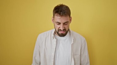 Kızgın, genç İspanyol bir adam, stresli ve bağırıyor, sarı izole bir arka plana karşı duruyor. Kameraya yakalanan öfkeli ifadenin portresi.