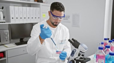 Laboratuvardaki sakallı adam laboratuarda pipet ve mikroskopla deney yapıyor.