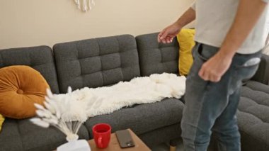 Sakallı, orta yaşlı bir adam rahat bir oturma odasındaki kanepede akıllı telefonunu kullanıyor..