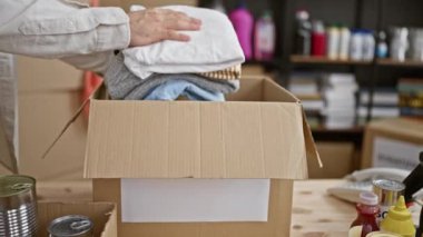 Yakışıklı, sakallı, İspanyol asıllı genç bir adamın gönüllü olarak hayır kurumunda çalışan, özenle çalışan ve toplum desteği için bağış yapan bir paketin içine giysiler koyan bir portresi..