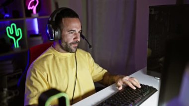 Geceleri neon ışıklı oyun odasında kulaklık takan sakallı yakışıklı İspanyol bir adam bilgisayar ekranına odaklanıyor..