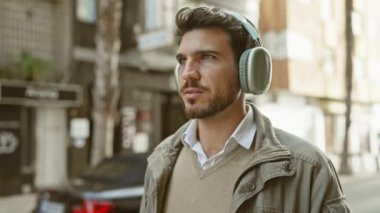Kulaklıklı yakışıklı İspanyol genç adam güneşli bir şehir sokağında müzik dinlemekten hoşlanıyor..