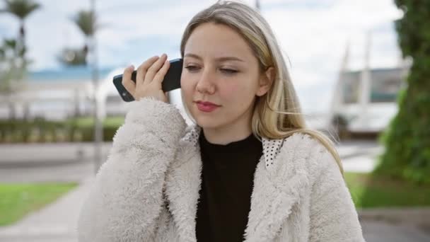 若い女性は緑豊かな屋外公園の設定でスマートフォンを使用し 近代的な接続性とレジャーを示しています — ストック動画