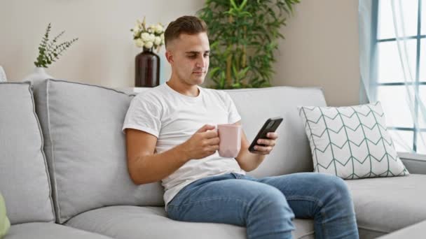 Hombre Joven Usando Teléfono Inteligente Sofá Con Taza Rosa Acogedora — Vídeo de stock
