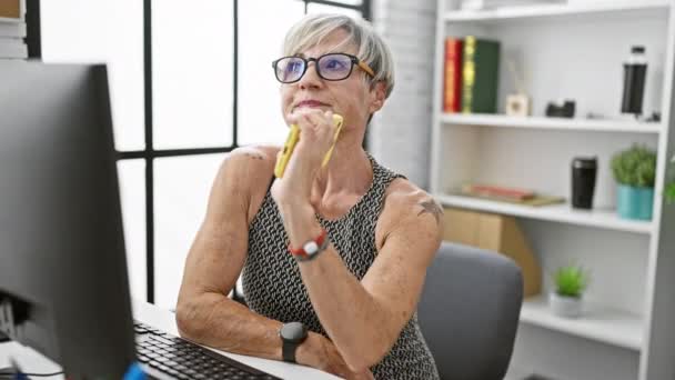 オフィスの設定でスマートフォンを使用したメガネと短い灰色の髪の思慮深い成熟した女性 — ストック動画