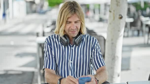 Mężczyzna Średnim Wieku Słuchawkami Słucha Muzyki Swoim Smartfonie Kawiarni Świeżym — Wideo stockowe