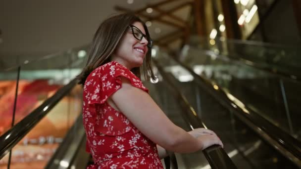モールエスカレーターにメガネをかけた陽気な美しいヒスパニックの女性が 都市中心部で買い物をしながらポジティブなオーラを放射します — ストック動画