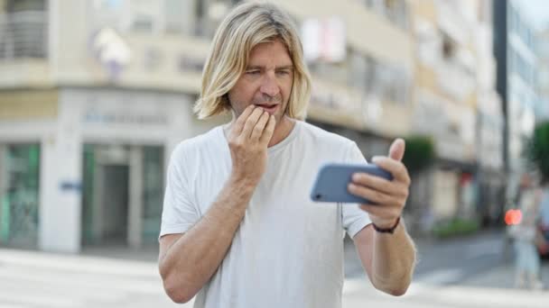 市街地のトランジションでスマートフォンを使用して懸念金髪の男成功ジェスチャーで興奮 — ストック動画