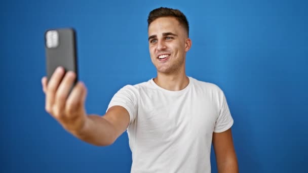 Young Man Takes Selfie Smiling Waving Vibrant Blue Wall Background — Stock Video