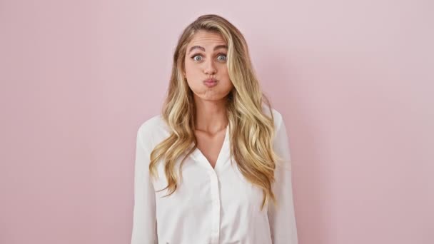 ピンクの背景に頬をふるう若い金髪の女性の複雑な肖像画 立って クレイジーな 面白い表情をクラッキング — ストック動画
