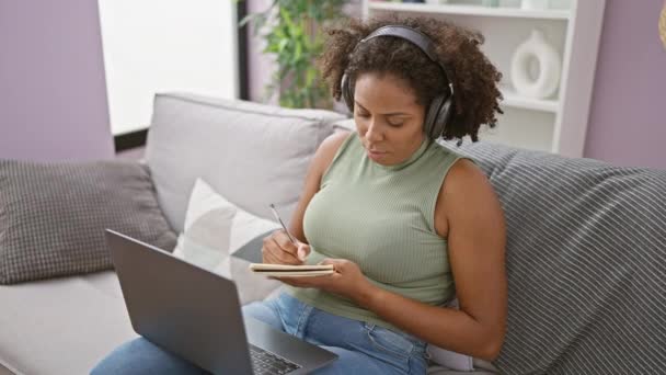 African American Woman Writing Notes Couch Laptop Headphones — Stock Video