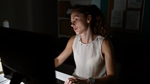 在黑暗的办公室内部从事计算机工作的重点年轻妇女 — 图库视频影像