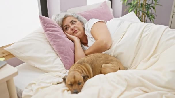 在舒适的卧室里 一个灰白头发的女人在她的宠物狗旁边的床上醒来 — 图库视频影像