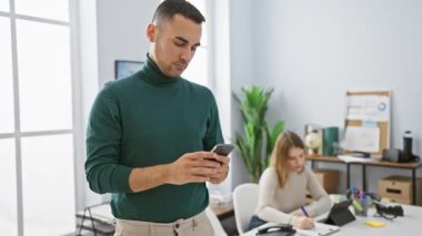 Akıllı telefon kullanan bir adam ve modern ofis içinde tabletle çalışan odaklanmış bir kadın..