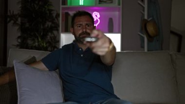 Akşamları modern oturma odasında kumandalı gri saçlı, olgun İspanyol bir adam.