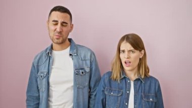 Güzel bir çift, yüzlerinde kuşkucu bir ifade, izole edilmiş pembe arka planda kot gömlekler içinde duruyorlar, şaşırdıklarını ve alaycı inançsızlıklarını ifade ediyorlar.