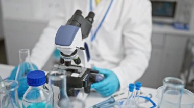 Gözlüklü ve sakallı bir bilim adamı laboratuvar ortamında mikroskop kullanarak araştırma yapıyor..