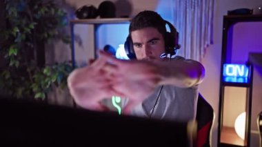 Kulaklık takan odaklanmış bir adam evdeki loş ışıklı bir oyun odasında bilgisayar kullanıyor..