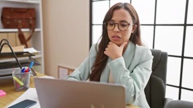 Neşeli genç bir profesyonel, güzel bir İspanyol kadın kendine güveni tam, başarılı işini şık bir ofisten yapıyor, dizüstü bilgisayar kullanıyor..