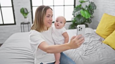 Anne, kızıyla yatakta oturmuş yatak odasında video görüşmesi yapıyor.