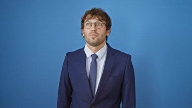 İş elbisesi içindeki afallamış genç adam, şaşırtıcı bir şekilde parmağıyla ileriyi işaret ediyor, ağzı açık huşu içinde. İzole edilmiş mavi arka plandaki bir şey onu şaşkına çeviriyor.!