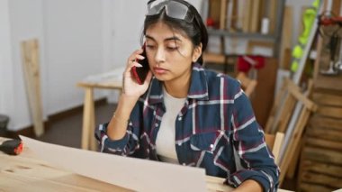 Marangozluk atölyesinde akıllı telefondan konuşan genç bir Güney Asyalı kadın....