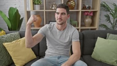 Kendine güvenen genç bir adam modern bir oturma odasında kaslarını esnetiyor, evde zindelik ve sağlığını gösteriyor..