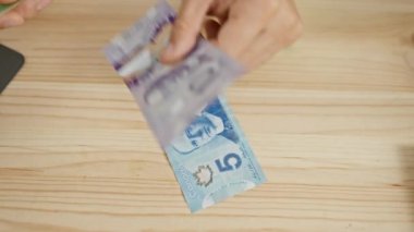 Ahşap bir yüzey üzerinde Kanada doları sayan bir el, bir marangozluk atölyesinde finans tasvir.