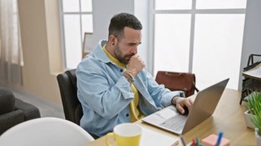 Modern ofis ortamında çalışan ve kahve içen sakallı bir adam odaklanma ve günlük iş kıyafetlerini gösteriyor..
