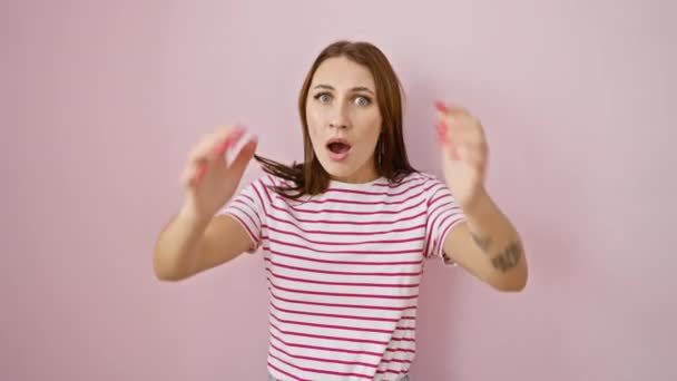 ストライプTシャツの若いブルネットガールはショックで頭を抱えています クレイジー怖い表現 ピンクの隔離された背景に驚きで広く開いた口 — ストック動画