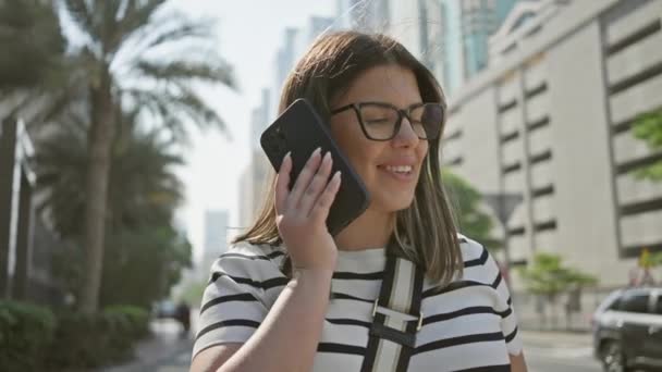 Μια Χαμογελαστή Νεαρή Γυναίκα Γυαλιά Μιλάει Ένα Smartphone Μια Ηλιόλουστη — Αρχείο Βίντεο