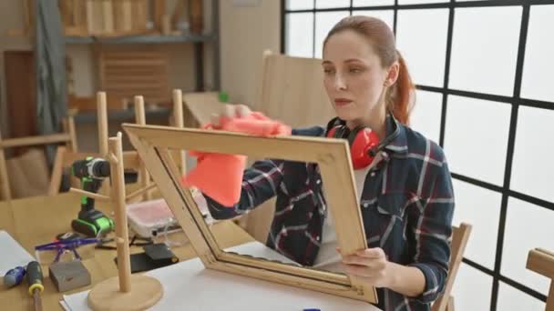 若い女性は 彼女の忠実で創造的な精神を反映した大工のワークショップで木製のフレームをきれいにします — ストック動画