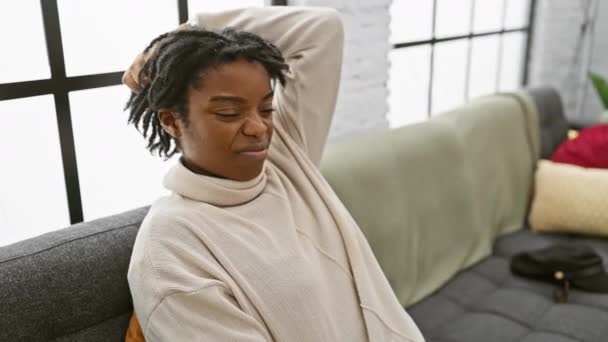 有思想的年轻黑人女人 留着可怕的头发 坐在家里的沙发上 苦苦思索着一个问题 她那令人怀疑的表情揭示出一种沉思的心情 一种好奇而又不确定的观念 — 图库视频影像
