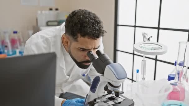 現代の実験室で顕微鏡の下で物質を検査する焦点を当てた若者 — ストック動画