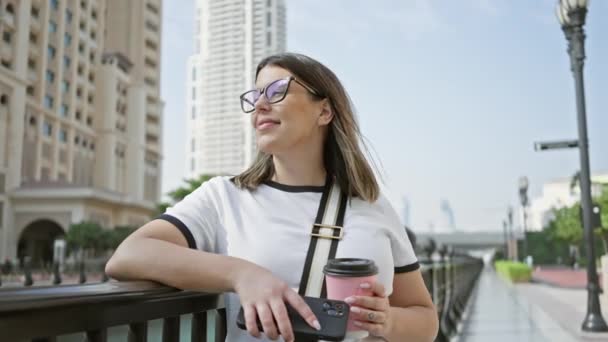 Młoda Dorosła Kobieta Okularach Kawą Smartfonem Balustradzie Nowoczesną Architekturą Katarską — Wideo stockowe