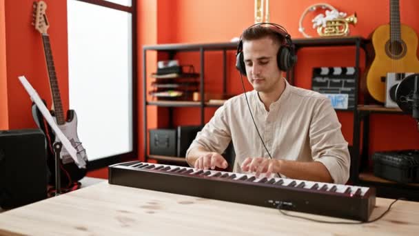 Молодой Латиноамериканец Играет Клавишных Музыкальной Студии Окруженный Гитарами Аудио Оборудованием — стоковое видео