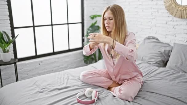 Pembe Pijamalı Genç Bir Kadın Yatakta Otururken Termometreyi Inceliyor Kulaklıkları — Stok video
