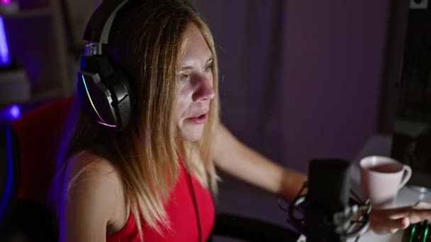 カラフルなヘッドセット マイク 目に見える熱意で夜に屋内でゲームするブロンドの女性 — ストック動画
